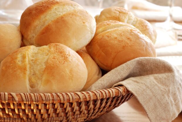 Fresh bread rolls in a woven basket with a cloth napkin on a wooden table