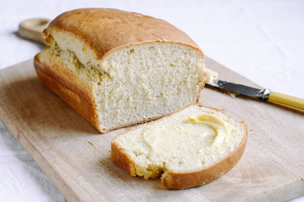 Fresh bread slice with butter spread on a wooden board showing soft bread texture