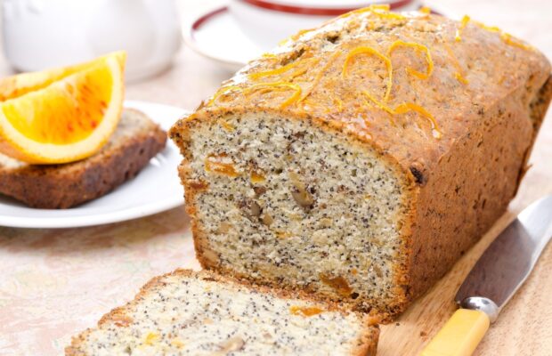 A close up of a loaf of citrus nut bread with slices served on a wooden board