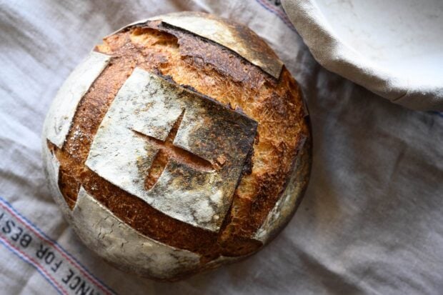 Rustic loaf of bread with a cross pattern on top placed on a cloth surface
