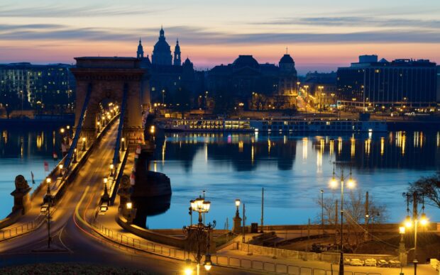 The historic Budapest bridge illuminated at dusk with the city skyline in the background