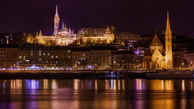 Illuminated Budapest buildings and Danube River at night with clear sky and calm water reflections