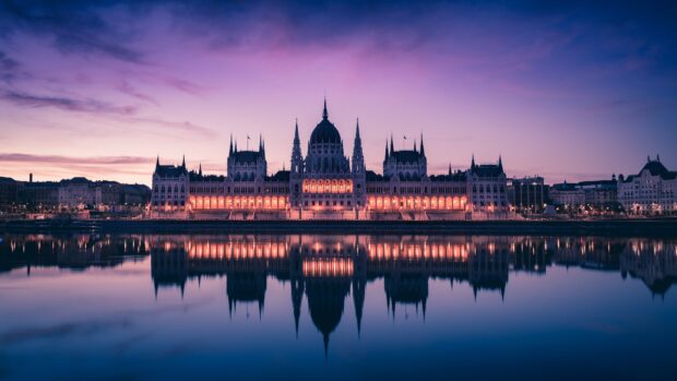 The Parliament building in Budapest reflects beautifully on the river at sunset with a clear sky