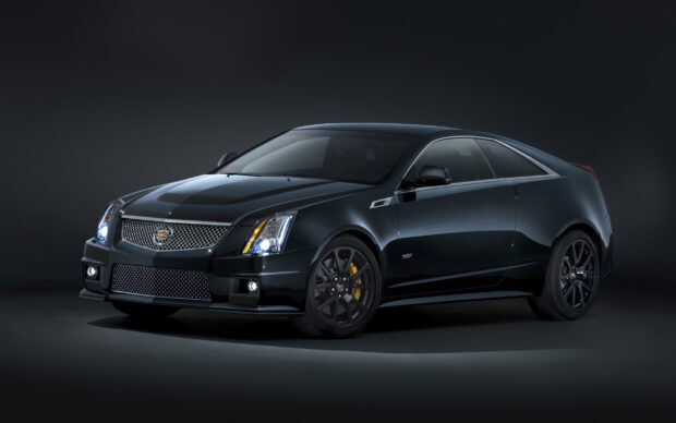 Black Cadillac sports car with headlights on in dark studio setting