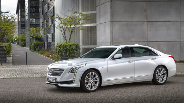 A sleek silver Cadillac parked on the street near modern buildings with greenery in the background
