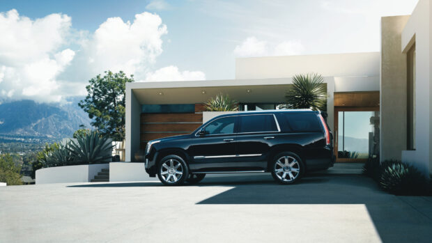 Black Cadillac parked driveway modern house with mountains background