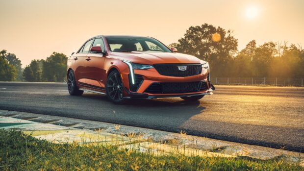 Orange Cadillac parked on a race track during sunset with trees in the background