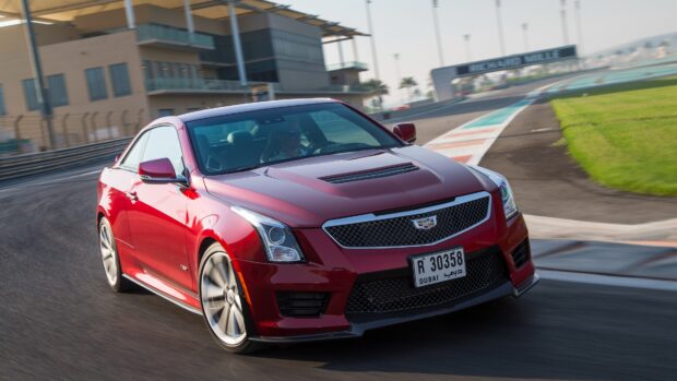 Red Cadillac car driving on racetrack with a Dubai license plate