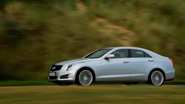 Silver Cadillac sedan driving fast on a blurred road with green background
