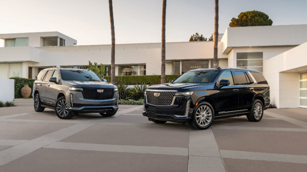 Two Cadillac SUVs parked in front of a modern house with palm trees in the background