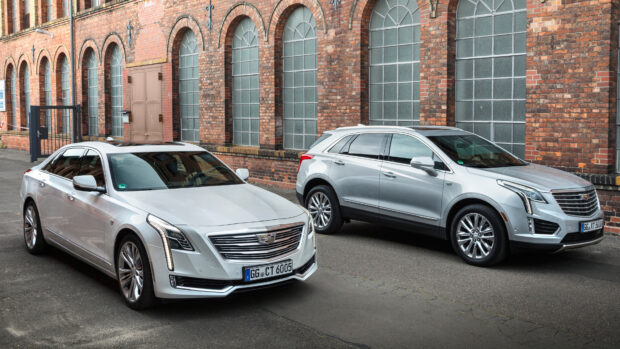 Two silver Cadillac cars parked beside a brick wall featuring classic arched windows