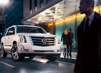 White Cadillac SUV parked on city street at night with people nearby