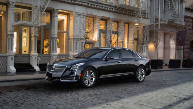 A black Cadillac parked on a cobblestone street in front of a historic building at dusk