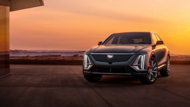 A sleek Cadillac with illuminated front grille parked at sunset in a desert setting