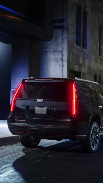 Black Cadillac vehicle tail lights glowing on a dark urban street at night
