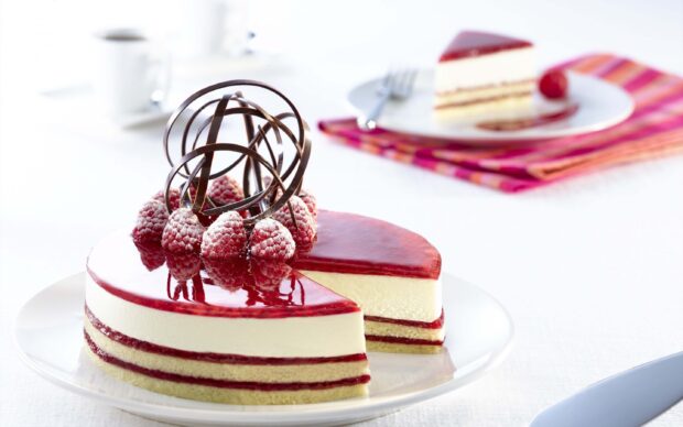 A creamy raspberry cake decorated with chocolate spirals and fresh raspberries on a white plate