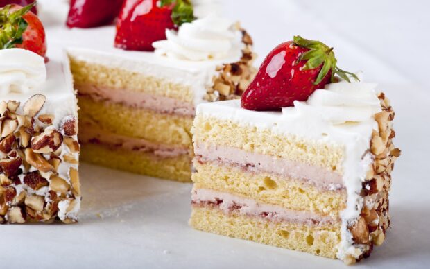 A slice of strawberry cake with cream and nut toppings on a white surface