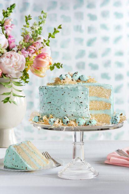 Blue cake with speckled eggs decoration and floral arrangement nearby