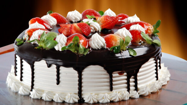 A delicious cake with strawberries and chocolate glaze topping on white cream frosting
