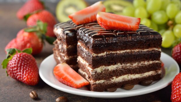 Chocolate cake slice with strawberry topping and grape background on plate