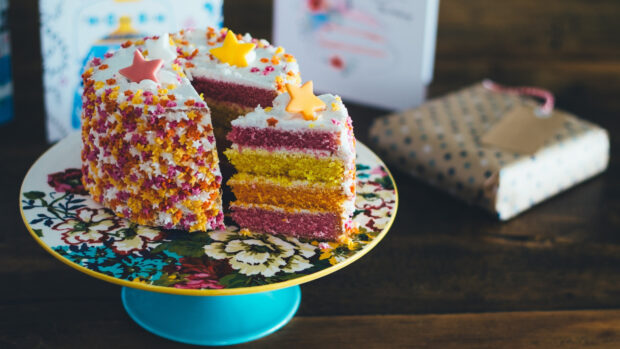 A colorful layered cake decorated with star shaped sprinkles on a floral plate
