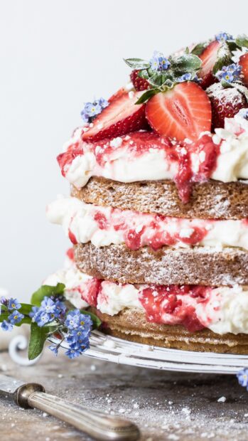 A layered cake with fresh strawberries and cream decorated with small blue flowers