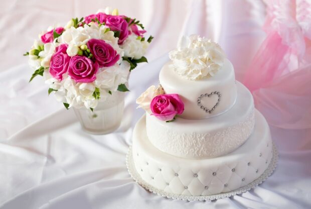 A beautiful cake decorated with white and pink roses next to a bouquet of pink and white flowers