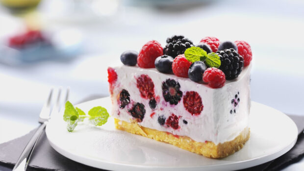 A creamy berry cake slice with raspberries blackberries and blueberries on a plate