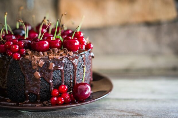 A chocolate cake decorated with fresh cherries and red currants on a dark plate