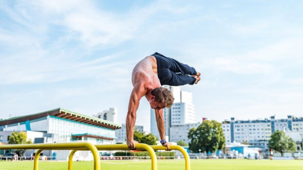 A man performing advanced calisthenics exercise on parallel bars outdoors