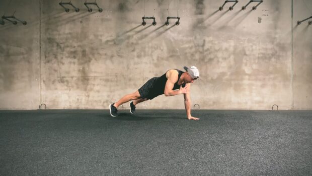 A man performing a calisthenics exercise in a gym with a concrete wall background