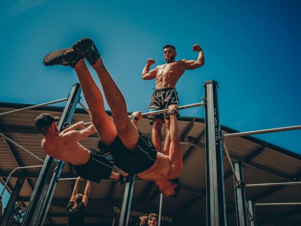 Muscular men performing advanced calisthenics exercises on pull up bars outdoors