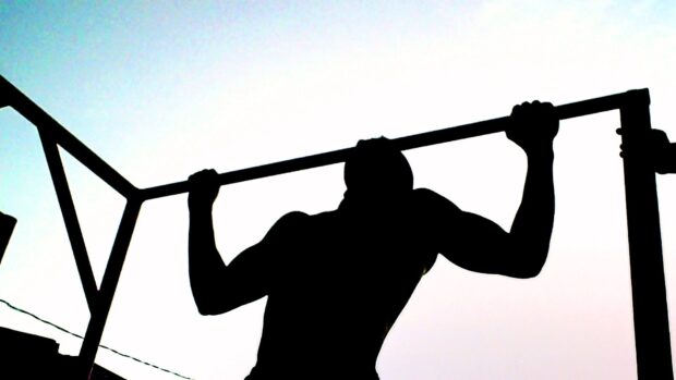 A person performing calisthenics pull up exercise on a horizontal bar during sunset