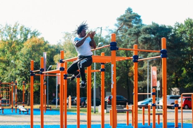 Athletic man performing calisthenics jump on outdoor bars in a park