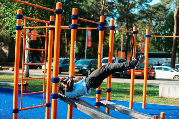 Man performing calisthenics exercise on outdoor gym bars in a park