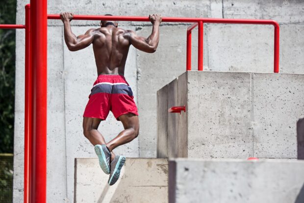 Muscular man performing calisthenics exercise on a red pull up bar outdoors