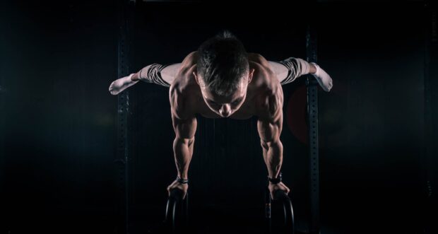 Muscular man performing calisthenics exercise on parallel bars in dark gym environment