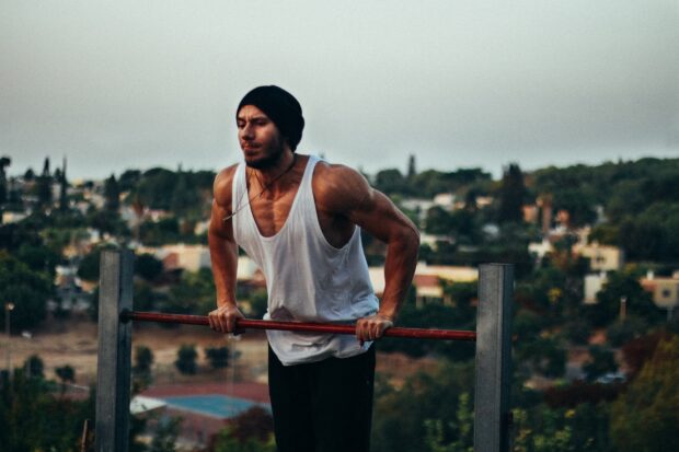 Muscular man performing calisthenics exercise on parallel bars outdoors