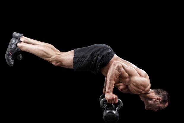 Muscular man performing calisthenics exercise with kettlebell on black background