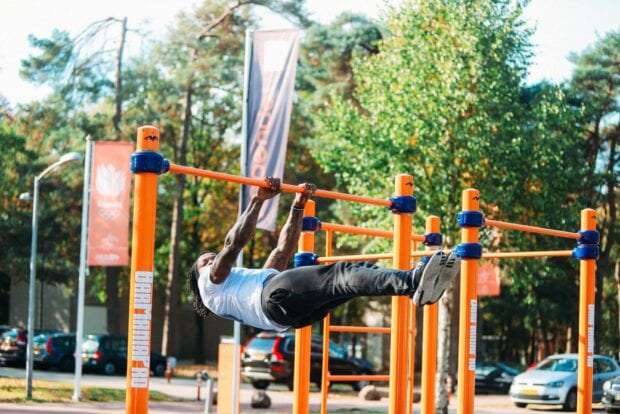 A man demonstrating calisthenics strength on orange bars in an outdoor park