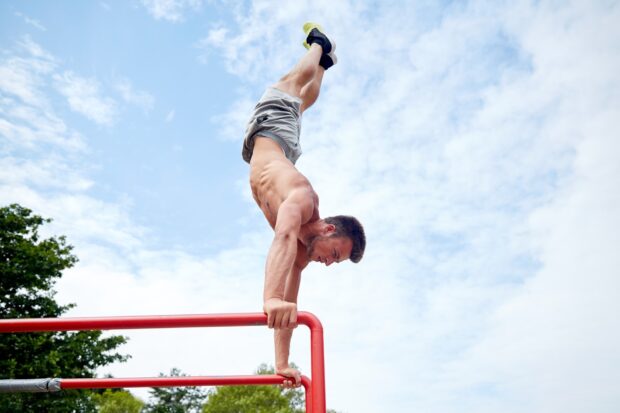 Muscular man performing calisthenics handstand on parallel bars outdoors
