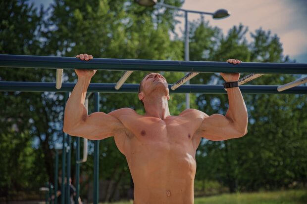 Muscular man performing calisthenics pull up exercise outdoors