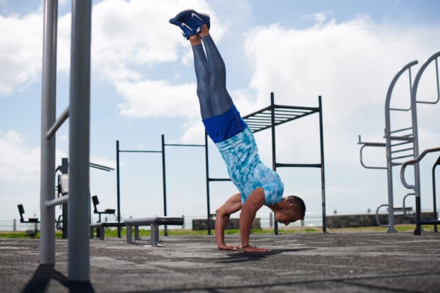 A man performing a handstand demonstrating calisthenics strength and balance at an outdoor gym