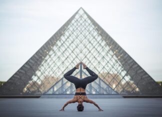 A person performing a calisthenics headstand pose in front of a glass pyramid building