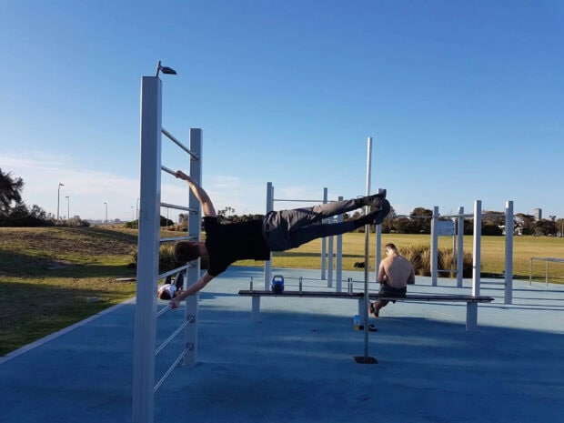 A man performing a human flag calisthenics exercise on outdoor bars in a park