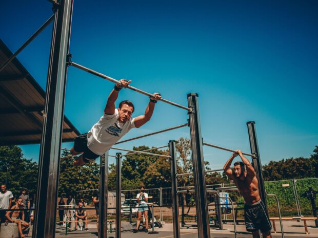 A man performing a muscle up on a bar during an outdoor calisthenics workout session