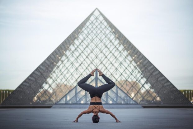 A person performing a calisthenics headstand pose in front of a glass pyramid building