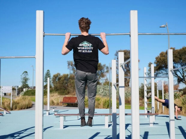 A man performing pull ups in an outdoor calisthenics training area under clear blue sky