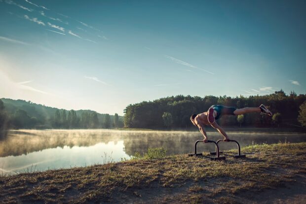 A man practicing calisthenics exercise outdoors by a lake using parallel bars