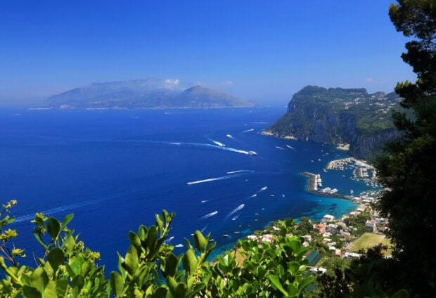 A scenic view of Capri Island with blue sea and lush greenery in the foreground